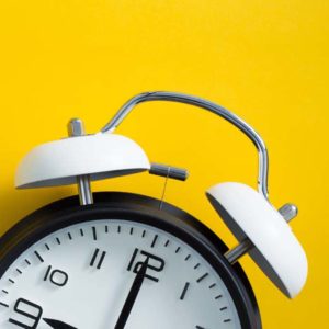 A close-up of a traditional black and white alarm clock against a bright yellow background showcases timeless design. The clocks hands point to 10:10, with its bells and handle clearly visible, capturing the essence of simplicity and precision akin to Ashevilles artisanal charm.
