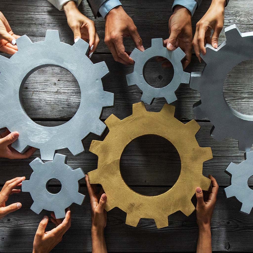 Hands of diverse people holding interconnected wooden gears on a wooden table, symbolizing teamwork and collaboration, much like a well-coordinated digital marketing team in Asheville, each gear representing a vital component of content management working seamlessly together.