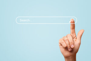 A hand with an extended index finger is about to press the search button in a digital search bar on a light blue background. The search bar contains the text Search....
