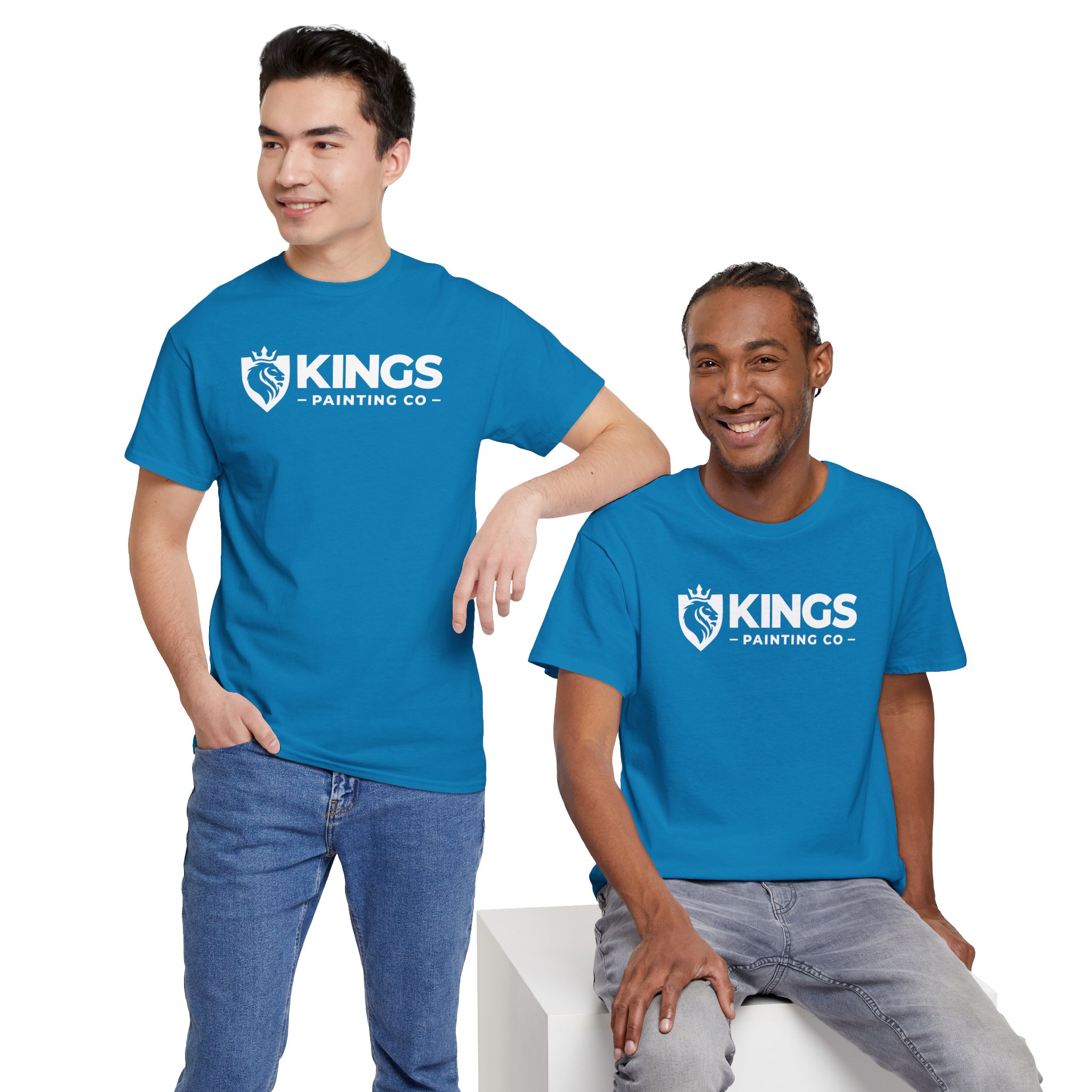 Two men wearing Kings Painting Co. Logo T‑Shirts (Classic) made from Gildan Ultra Cotton (G5000) in bright blue are smiling. One stands with a hand in his pocket while the other sits casually on a white block, both appearing relaxed and friendly.